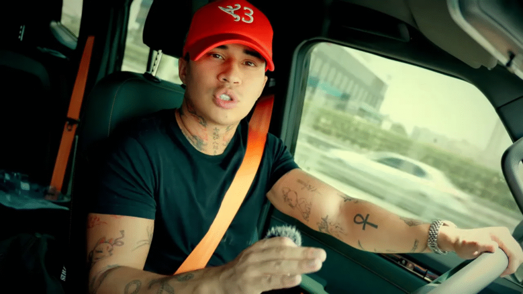 Auteur parlant directement à la caméra depuis le siège conducteur, casquette rouge, geste expressif