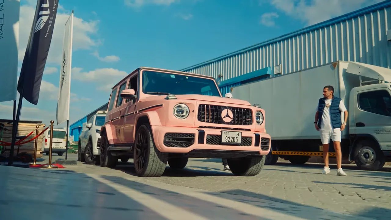 G-Wagon Mercedes rose garé devant un hangar avec des personnes autour