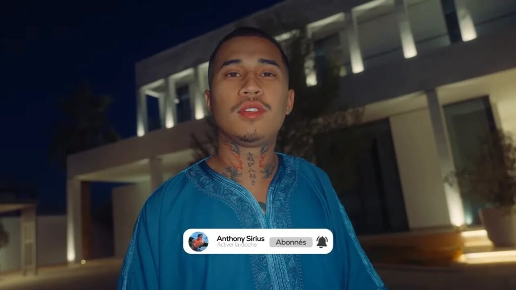 Anthony Sirius debout devant une maison éclairée la nuit, ambiance tôt le matin