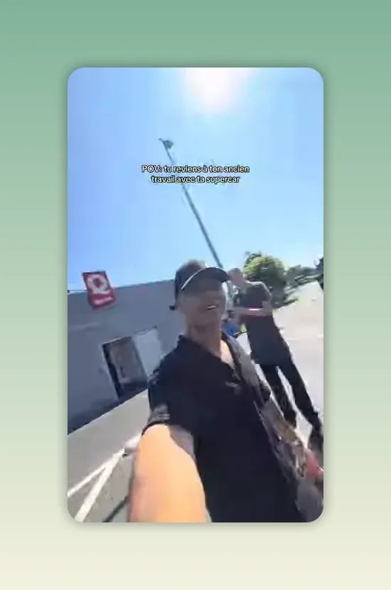 Un homme en casquette noire tend le bras pour filmer à côté d'un homme portant un tablier blanc sur un parking ensoleillé