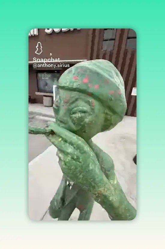 Statue verte d extraterrestre avec de grands yeux et une main près de la bouche devant un bâtiment